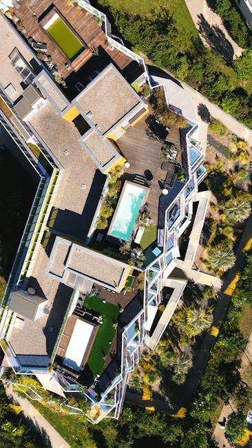 An aerial view of a modern residential rooftop garden attached to a multi-story building, featuring a central rectangular swimming pool with crystal-clear blue water and a surrounding wooden deck area